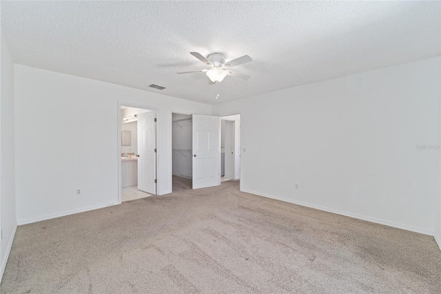 unfurnished bedroom with a spacious closet, light carpet, ceiling fan, connected bathroom, and a closet