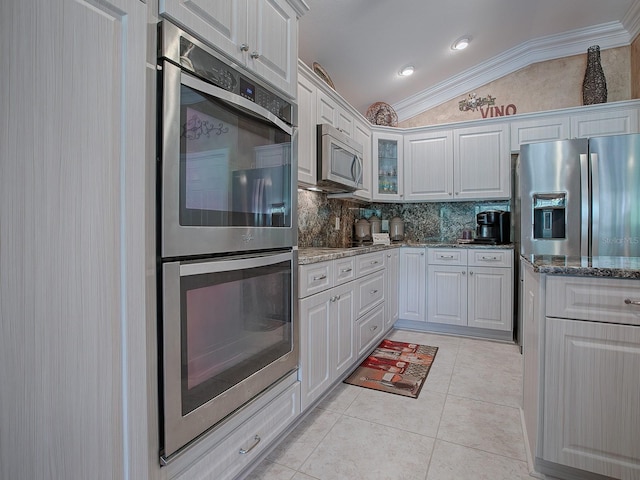 kitchen featuring tasteful backsplash, dark stone counters, vaulted ceiling, white cabinets, and appliances with stainless steel finishes