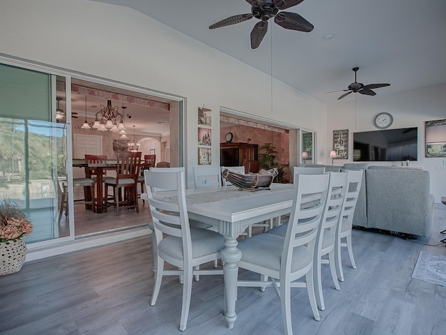 dining space with ceiling fan with notable chandelier, wood-type flooring, and lofted ceiling