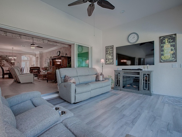 living room with ceiling fan with notable chandelier, a fireplace, light wood-type flooring, and crown molding