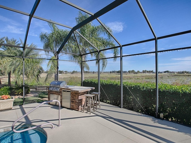 view of patio featuring a lanai, exterior kitchen, a bar, a rural view, and grilling area