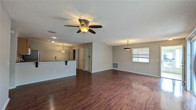 unfurnished living room with dark wood-type flooring, a textured ceiling, and ceiling fan