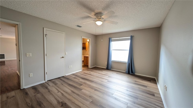 unfurnished bedroom featuring ceiling fan, light hardwood / wood-style floors, a textured ceiling, and ensuite bathroom