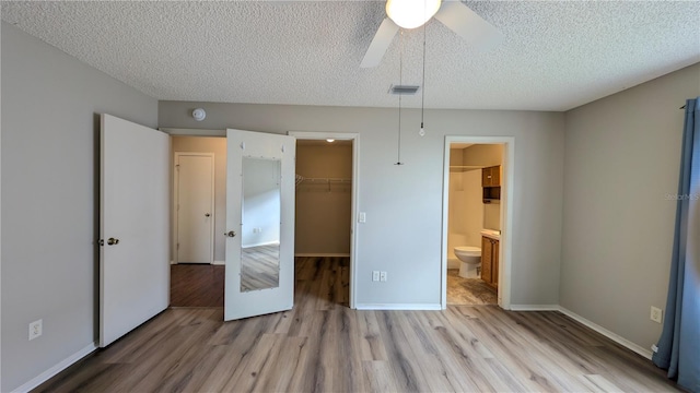 unfurnished bedroom with a spacious closet, light hardwood / wood-style floors, a closet, and a textured ceiling