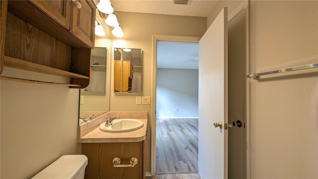 bathroom with hardwood / wood-style flooring, vanity, toilet, and a textured ceiling