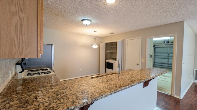 3449 Roanoke St, The Villages, FL 32162 - kitchen with a breakfast bar area, dark wood-style flooring, a sink, washer / clothes dryer, and light stone countertops