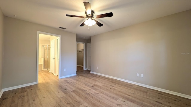 unfurnished bedroom featuring ensuite bath, light hardwood / wood-style flooring, ceiling fan, a walk in closet, and a closet