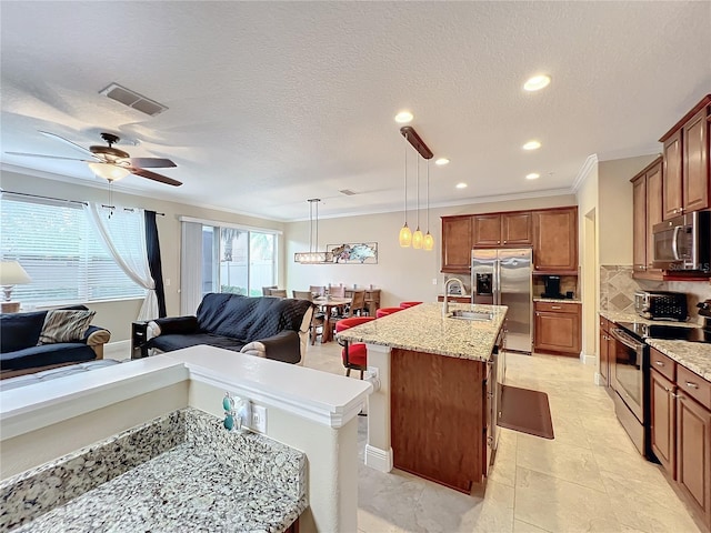 kitchen featuring a breakfast bar area, ornamental molding, an island with sink, decorative light fixtures, and stainless steel appliances