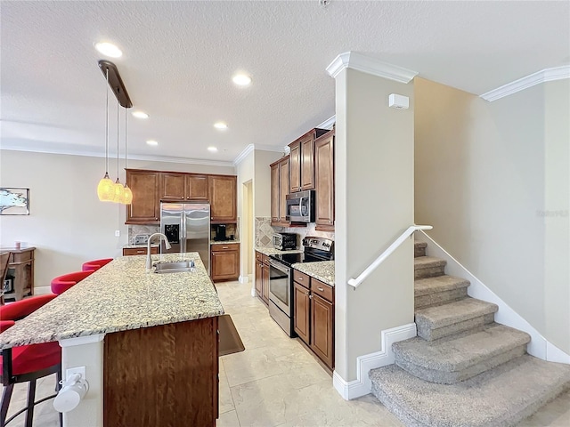 kitchen featuring appliances with stainless steel finishes, backsplash, sink, decorative light fixtures, and an island with sink