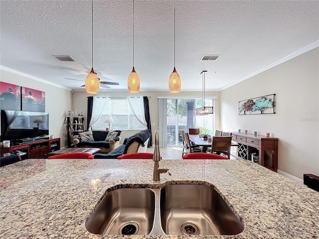 kitchen featuring a textured ceiling, crown molding, light stone countertops, and sink