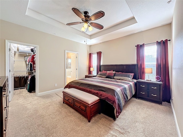 carpeted bedroom featuring a raised ceiling, a walk in closet, ceiling fan, and ensuite bath