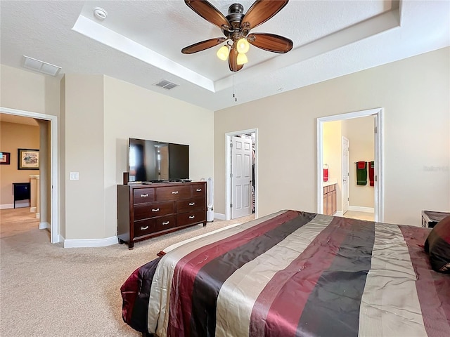 bedroom with light carpet, ensuite bathroom, a textured ceiling, a raised ceiling, and ceiling fan