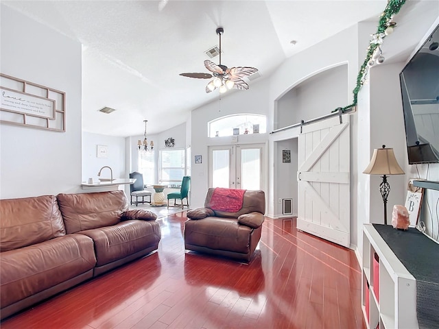 living room featuring french doors, ceiling fan with notable chandelier, vaulted ceiling, hardwood / wood-style flooring, and a barn door