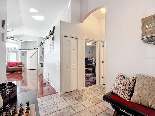 corridor featuring a barn door, light tile patterned flooring, and vaulted ceiling