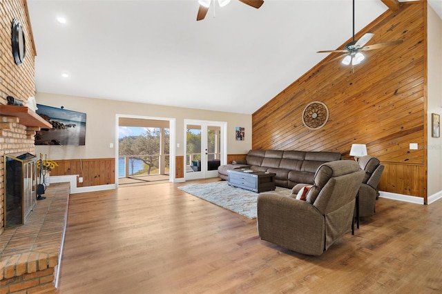 living room featuring wooden walls, ceiling fan, a fireplace, and high vaulted ceiling