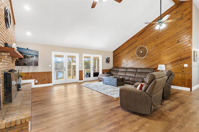 living room featuring french doors, high vaulted ceiling, a brick fireplace, and wood walls