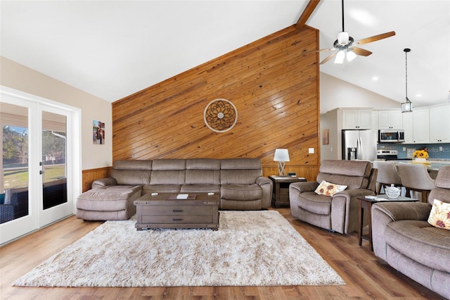 living room featuring wood walls, wood-type flooring, high vaulted ceiling, and french doors