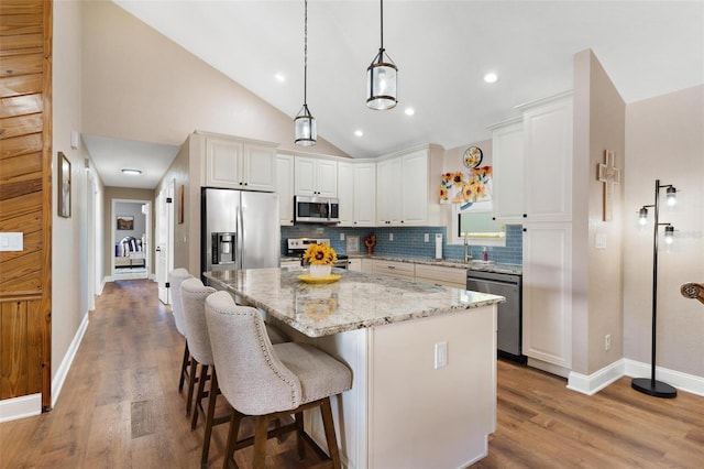 kitchen featuring backsplash, light stone counters, stainless steel appliances, a center island, and white cabinetry