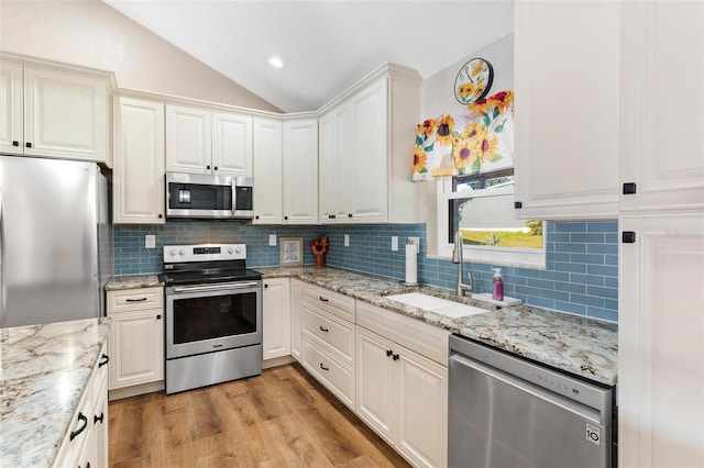 kitchen featuring lofted ceiling, white cabinets, light hardwood / wood-style flooring, light stone counters, and stainless steel appliances