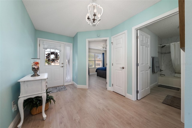 foyer entrance featuring a chandelier, light wood-type flooring, and a textured ceiling