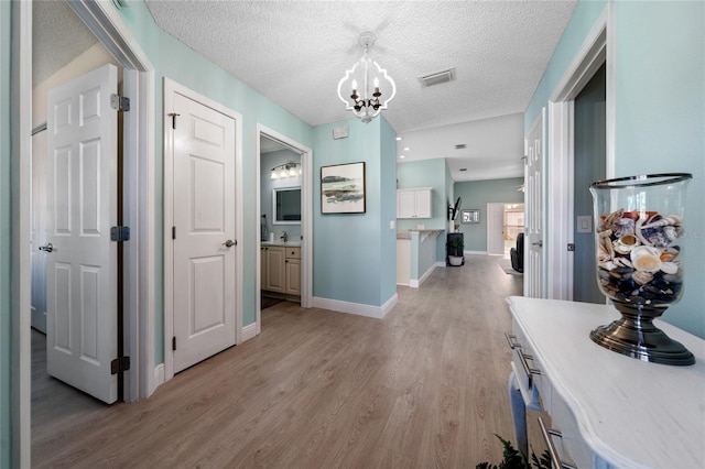 hallway featuring light hardwood / wood-style floors, a textured ceiling, and an inviting chandelier