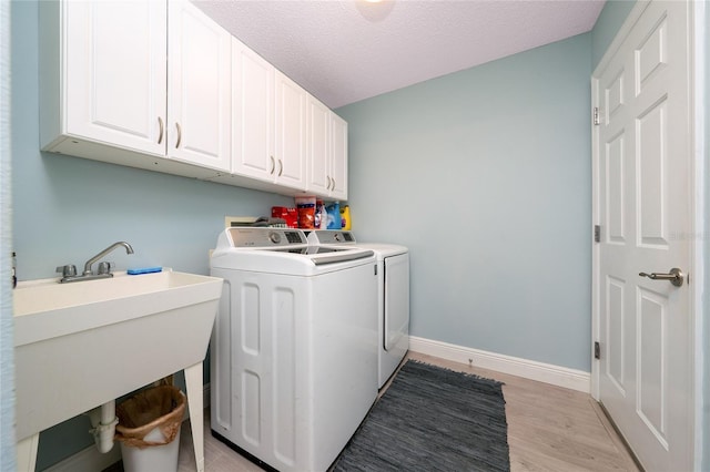 washroom featuring washer and dryer, sink, light wood-type flooring, a textured ceiling, and cabinets