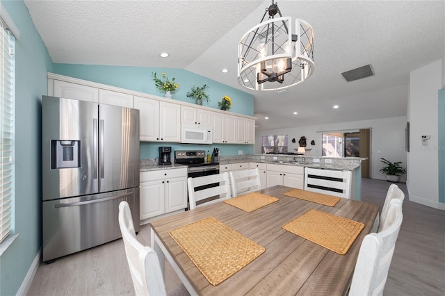 kitchen with stainless steel appliances, decorative light fixtures, vaulted ceiling, a chandelier, and white cabinets