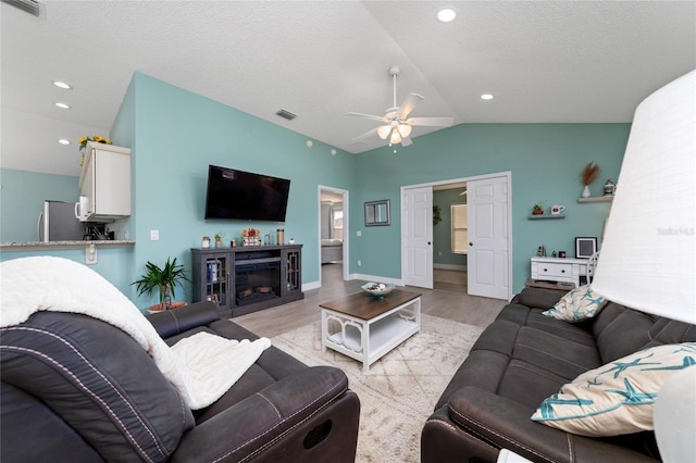 living room with ceiling fan, a textured ceiling, a fireplace, vaulted ceiling, and light hardwood / wood-style flooring