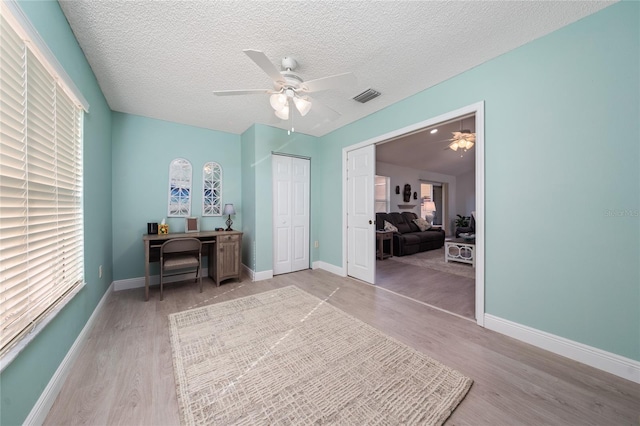 office featuring a textured ceiling, ceiling fan, a wealth of natural light, and light hardwood / wood-style flooring