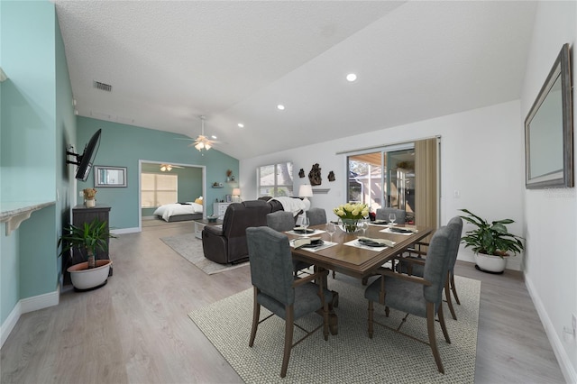 dining room with light wood-type flooring, vaulted ceiling, ceiling fan, and a textured ceiling