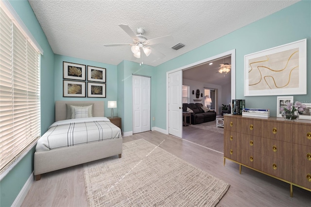 bedroom with light hardwood / wood-style floors, a closet, ceiling fan, and a textured ceiling