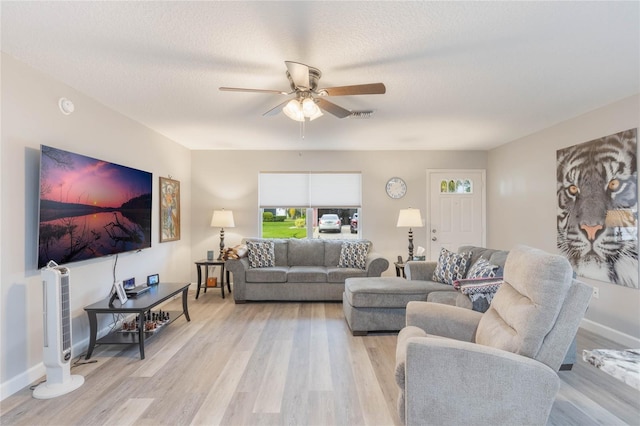 living room featuring ceiling fan, light wood-type flooring, and a textured ceiling