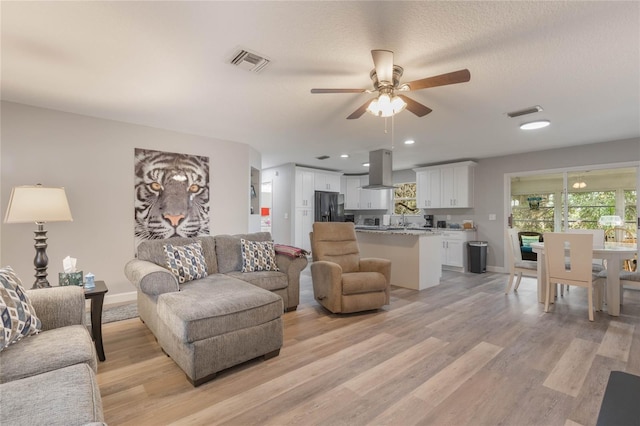 living room with ceiling fan, light hardwood / wood-style floors, and a textured ceiling