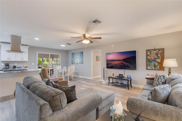 living room featuring a textured ceiling, light hardwood / wood-style floors, and ceiling fan