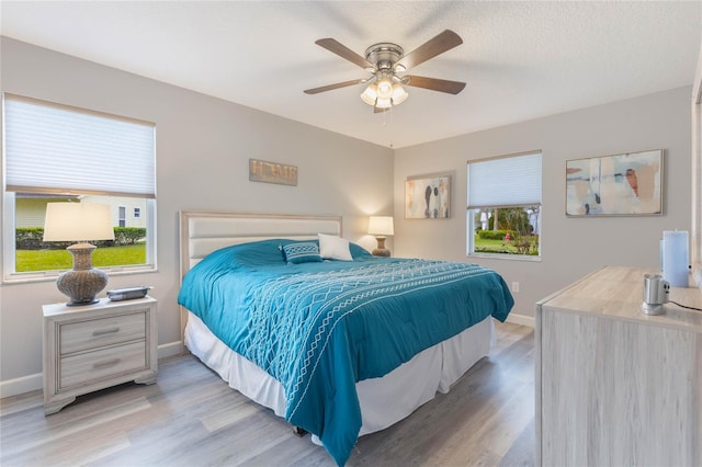 bedroom featuring multiple windows, a textured ceiling, light hardwood / wood-style floors, and ceiling fan