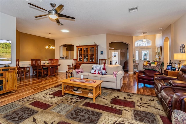 living room featuring hardwood / wood-style floors, ceiling fan with notable chandelier, and a textured ceiling