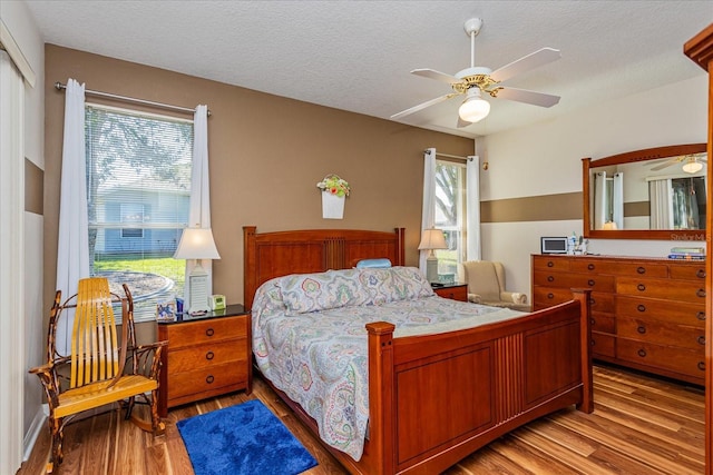 bedroom with ceiling fan, light wood-type flooring, and a textured ceiling