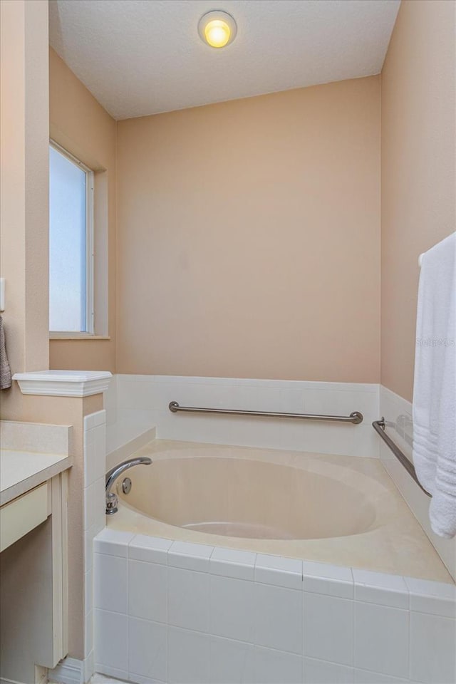 bathroom with tiled bath, vanity, and a textured ceiling