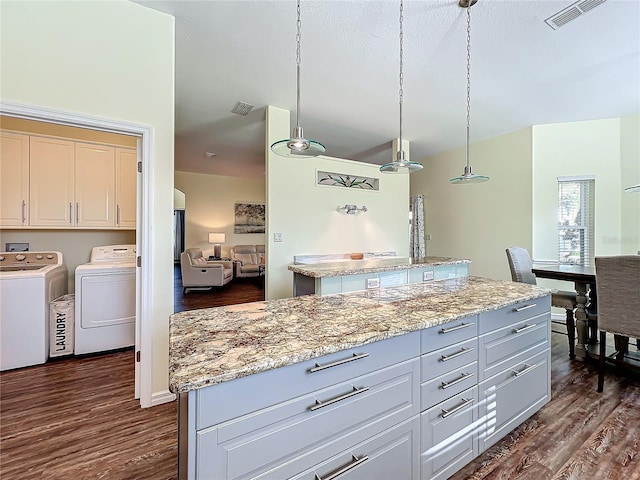 kitchen featuring washing machine and dryer, white cabinetry, a kitchen island, and hanging light fixtures