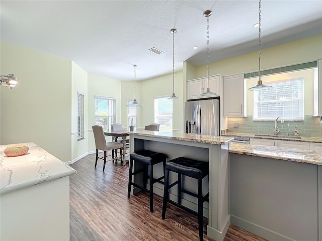 kitchen featuring a center island, hanging light fixtures, tasteful backsplash, stainless steel refrigerator with ice dispenser, and white cabinets