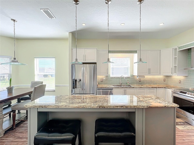 kitchen featuring white cabinets, decorative light fixtures, a center island, and stainless steel appliances