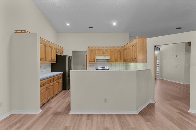 kitchen with appliances with stainless steel finishes, light brown cabinetry, backsplash, kitchen peninsula, and light hardwood / wood-style flooring