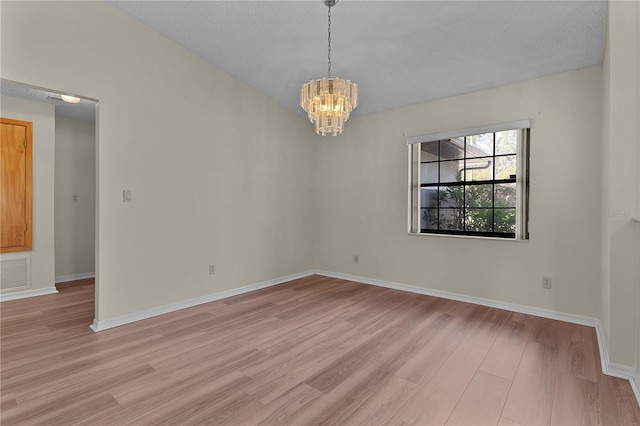 spare room with an inviting chandelier and light hardwood / wood-style floors