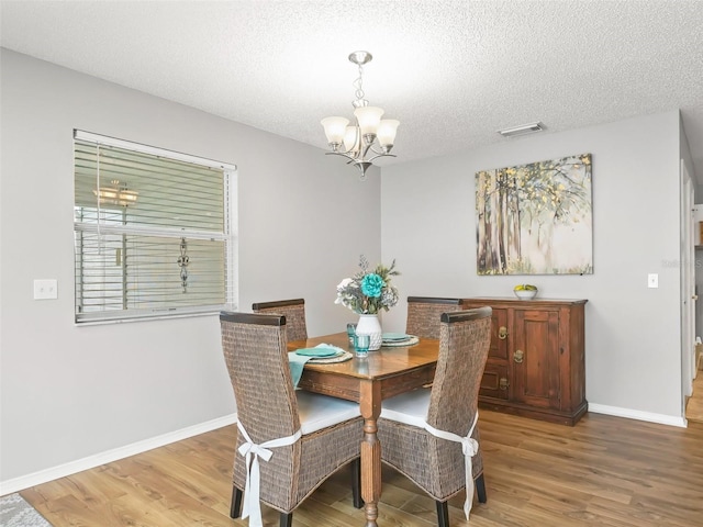 dining space with hardwood / wood-style flooring, a textured ceiling, and a chandelier