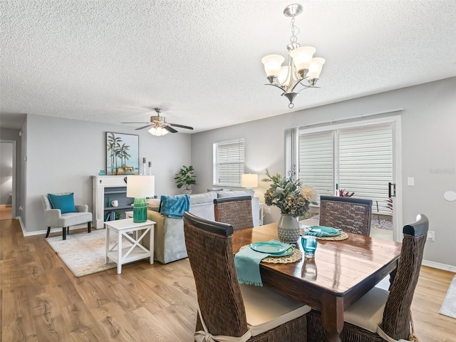 dining room with ceiling fan with notable chandelier, a textured ceiling, and light wood-type flooring