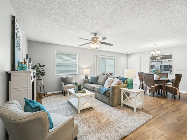 living room featuring ceiling fan with notable chandelier, a textured ceiling, and light hardwood / wood-style flooring