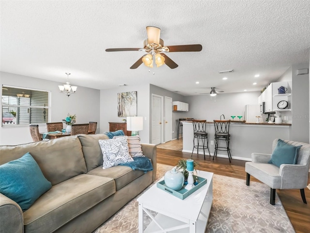 living room featuring a textured ceiling, ceiling fan with notable chandelier, and light hardwood / wood-style floors