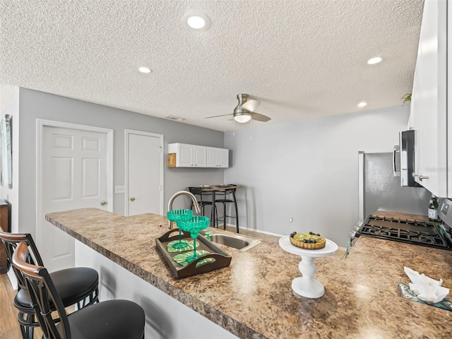 kitchen featuring ceiling fan, white cabinets, a kitchen breakfast bar, and a textured ceiling