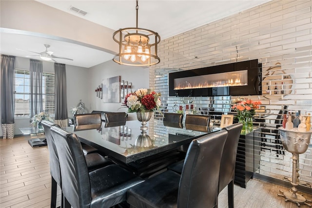 dining room with ceiling fan with notable chandelier and brick wall