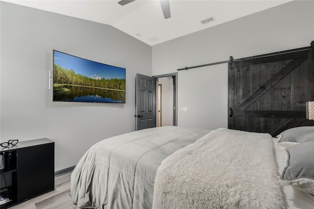 bedroom with ceiling fan, a barn door, vaulted ceiling, and light hardwood / wood-style flooring